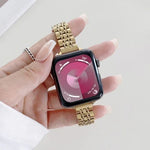 Hand holding an Apple Watch with a steel replacement strap for Apple Watch, displaying a pink watch face.